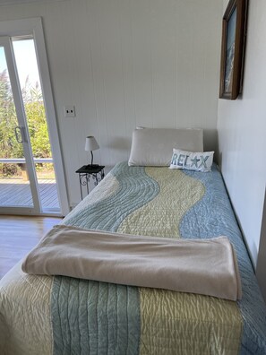 A bedroom with a bed, a pillow with 'RELAX' text, a lamp, and a view through a door to an outdoor area. - Waterfront Home on Beautiful Lake Tashmoo (Tisbury)
