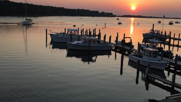 Een jachthaven met boten aan houten steigers tijdens zonsondergang.