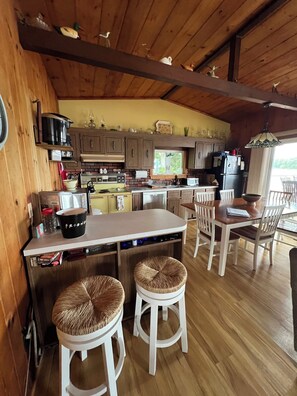 A wooden interior with a kitchen area, a dining table with chairs, and a bar stool.