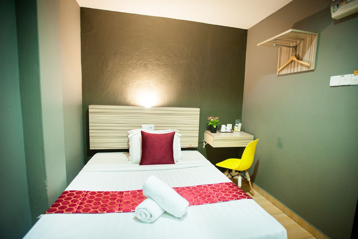 Habitació d'hotel amb un llit, una taula, una cadira i una prestatgeria penjada a la paret.