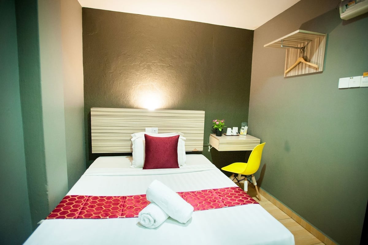Una habitació d'hotel amb llit, una taula de nit, una cadira i una estanteria penjada a la paret.