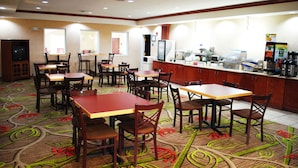 Un restaurante con varias mesas y sillas, una barra con máquina de café y un refrigerador.