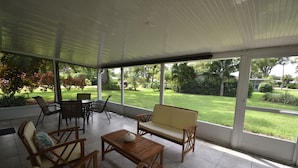 A covered patio area with wooden furniture, including a sofa, chairs, and a table.