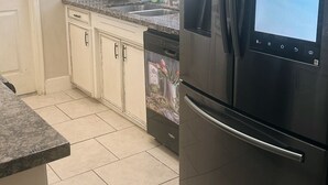 A kitchen with a black refrigerator, a dishwasher, and a window with blinds. - Charming home in sugarland (Sugar Land)