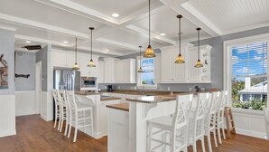 Una cocina amplia con armarios blancos, una isla central con taburetes altos e iluminación colgante.