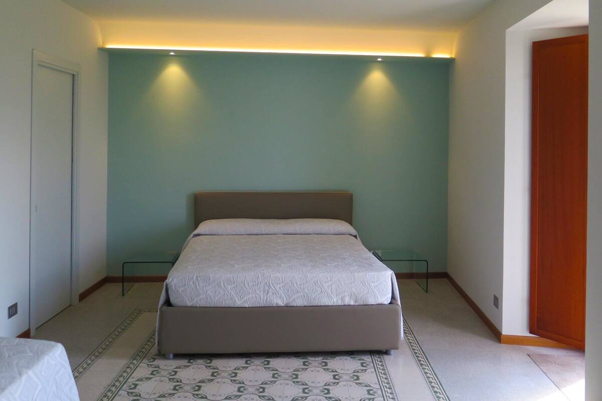 A bedroom with a bed, a nightstand, a wooden door, and a light strip above the bed.