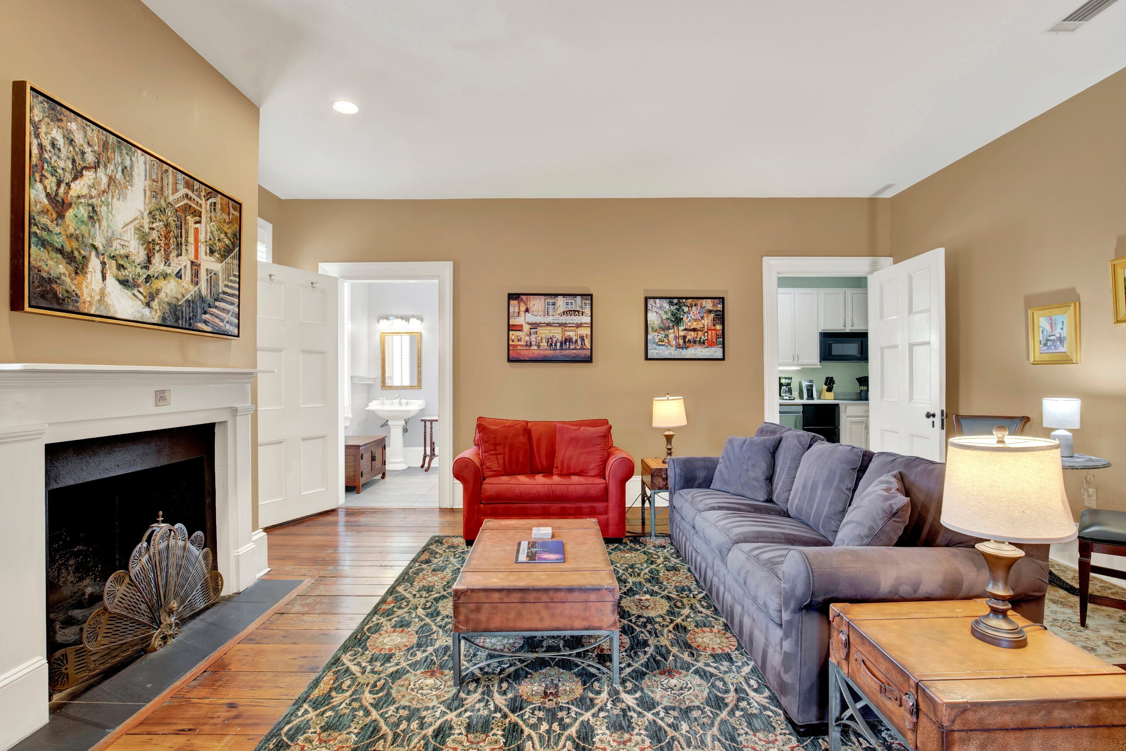 A living room with a fireplace, a red sofa, a grey sofa, a patterned rug, and a lamp.