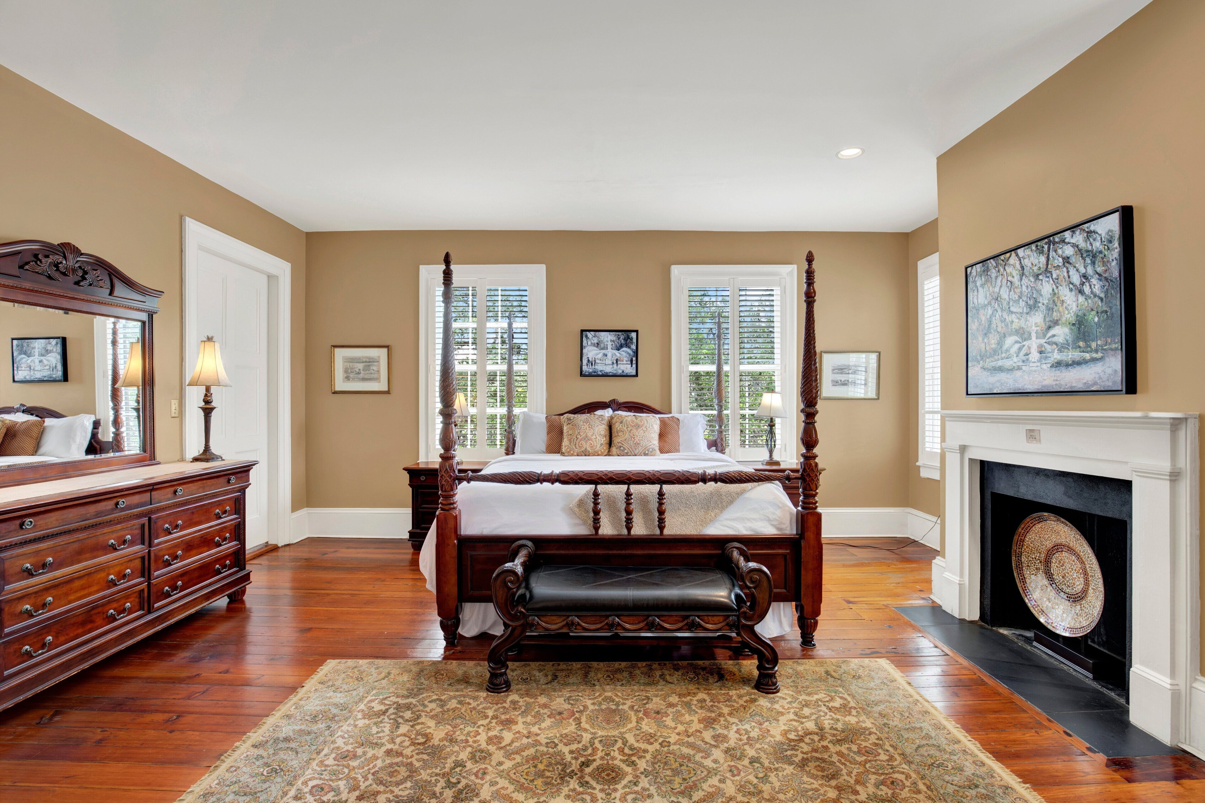 A bedroom with a four-poster bed, a dresser, a fireplace, and framed pictures on the walls.