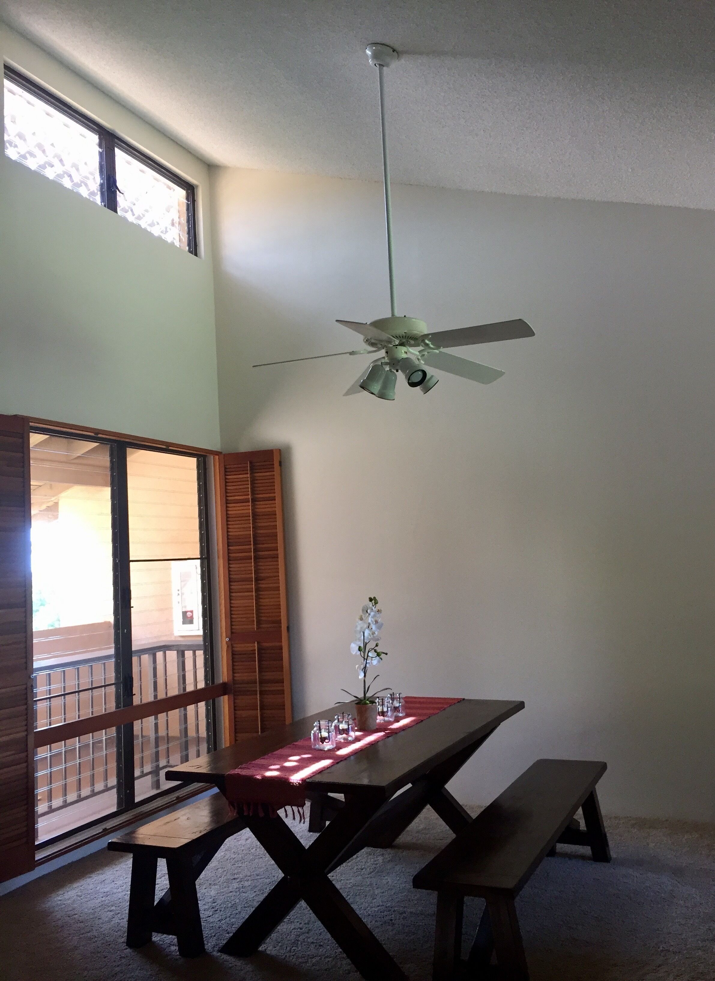 Un espace repas comprenant une table, des bancs, un ventilateur de plafond et une vue à travers une porte coulissante.