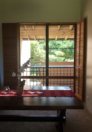 Una habitación con puerta corredera que da a un balcón exterior, una mesa de madera con un tapete rojo y una planta en maceta.
