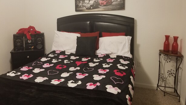 A bed with a black and white heart-patterned bedspread, a red plush toy, and a black headboard. There is a framed picture of a building on the wall above the bed.