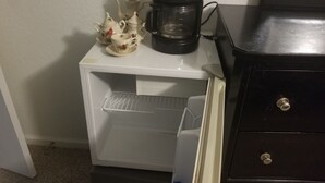 A small white refrigerator with a coffee maker on top, a water bottle, and a decorative tea set.