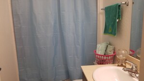 A bathroom with a blue shower curtain, a white sink, a toilet, and a pink basket with towels.