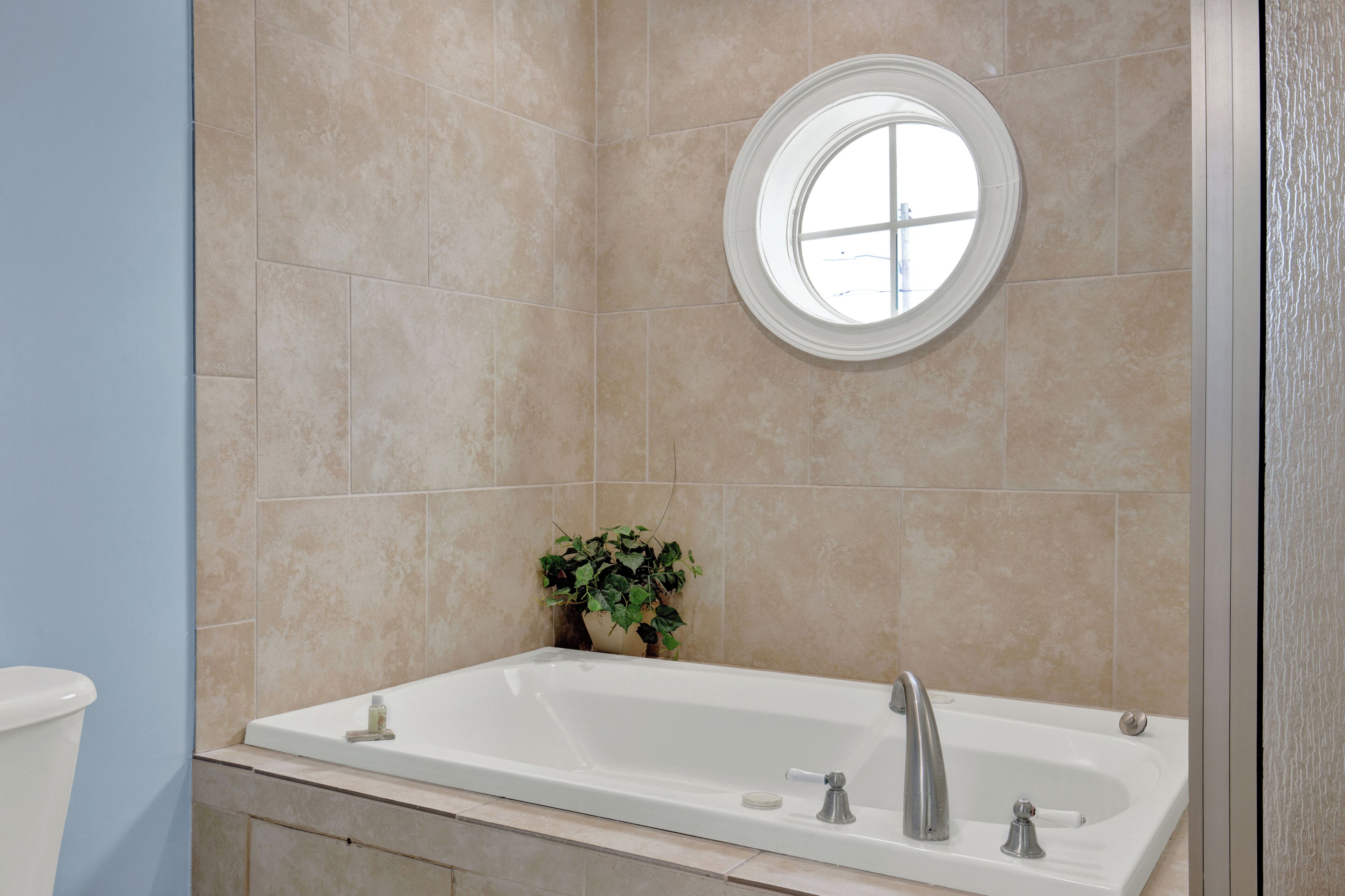 Une salle de bain avec une baignoire, une fenêtre ronde et une plante en pot.