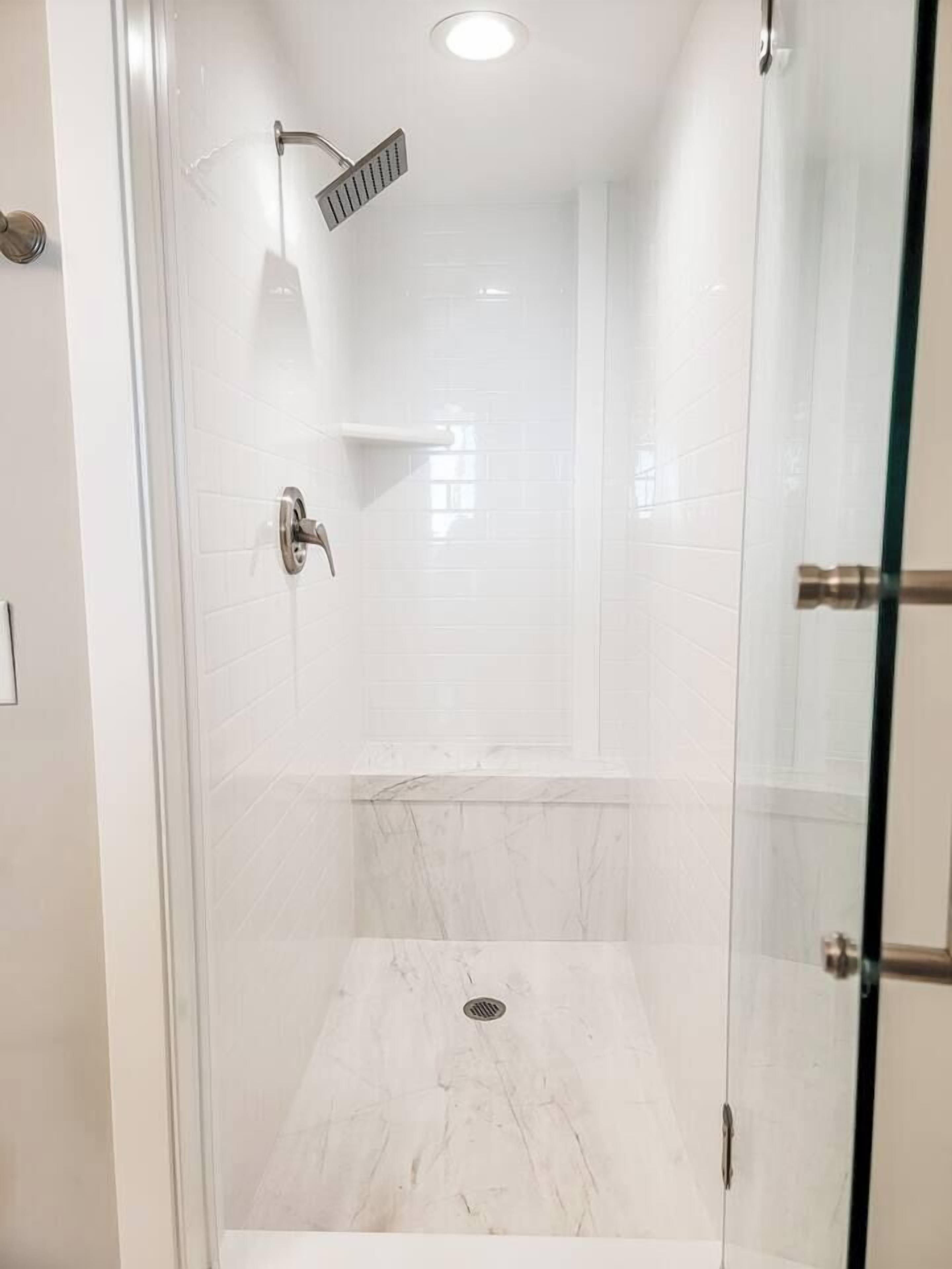 A modern shower with a glass door, a handheld showerhead, and a marble floor.
