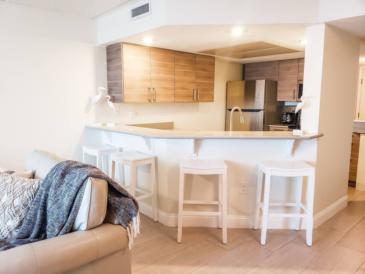 Eine moderne Küche mit Holzschränken, einer zentralen Kochinsel mit Sitzgelegenheiten und einem Kühlschrank.