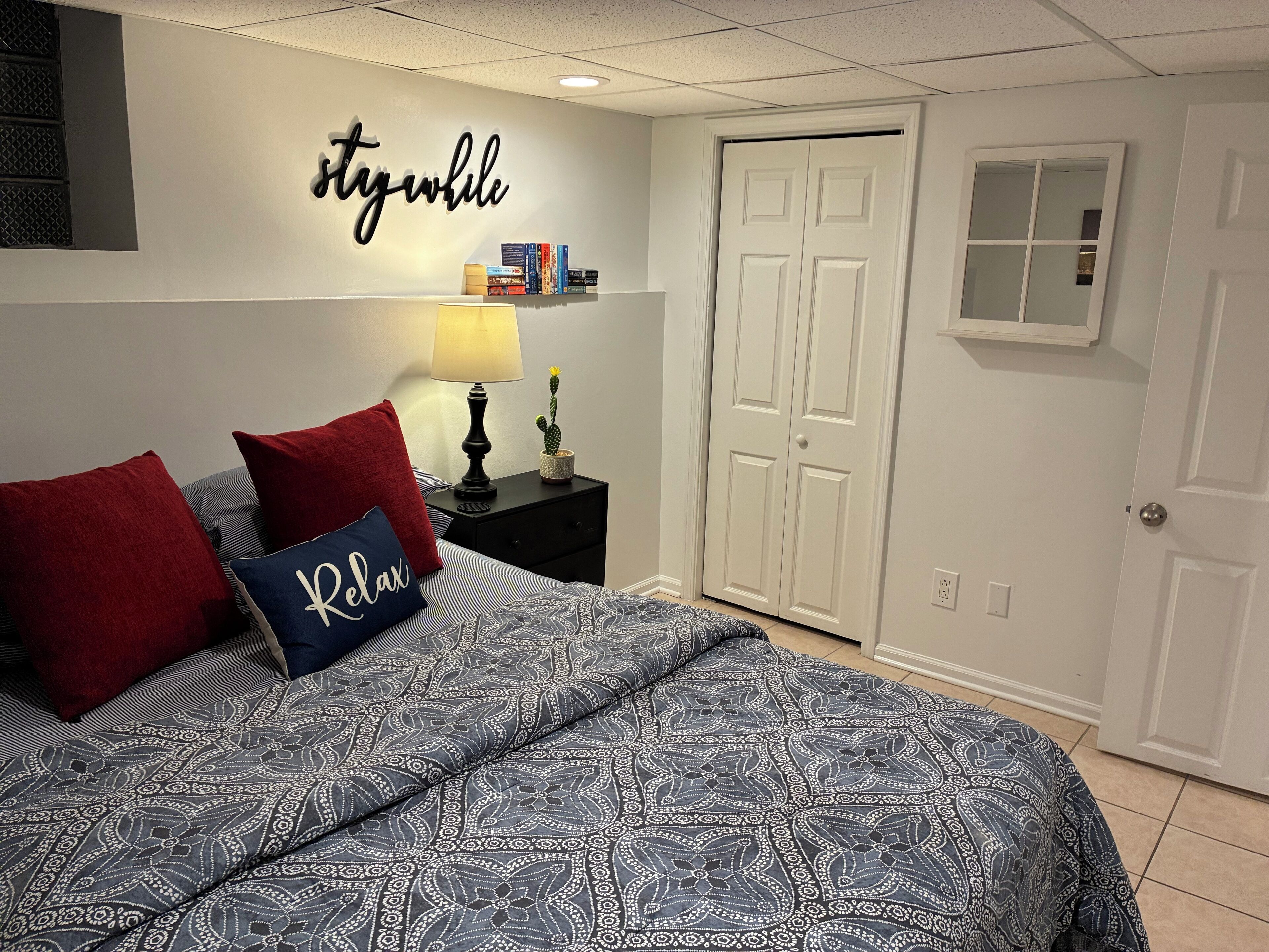 A bedroom with a bed, a nightstand, a lamp, a cactus, and a wardrobe.