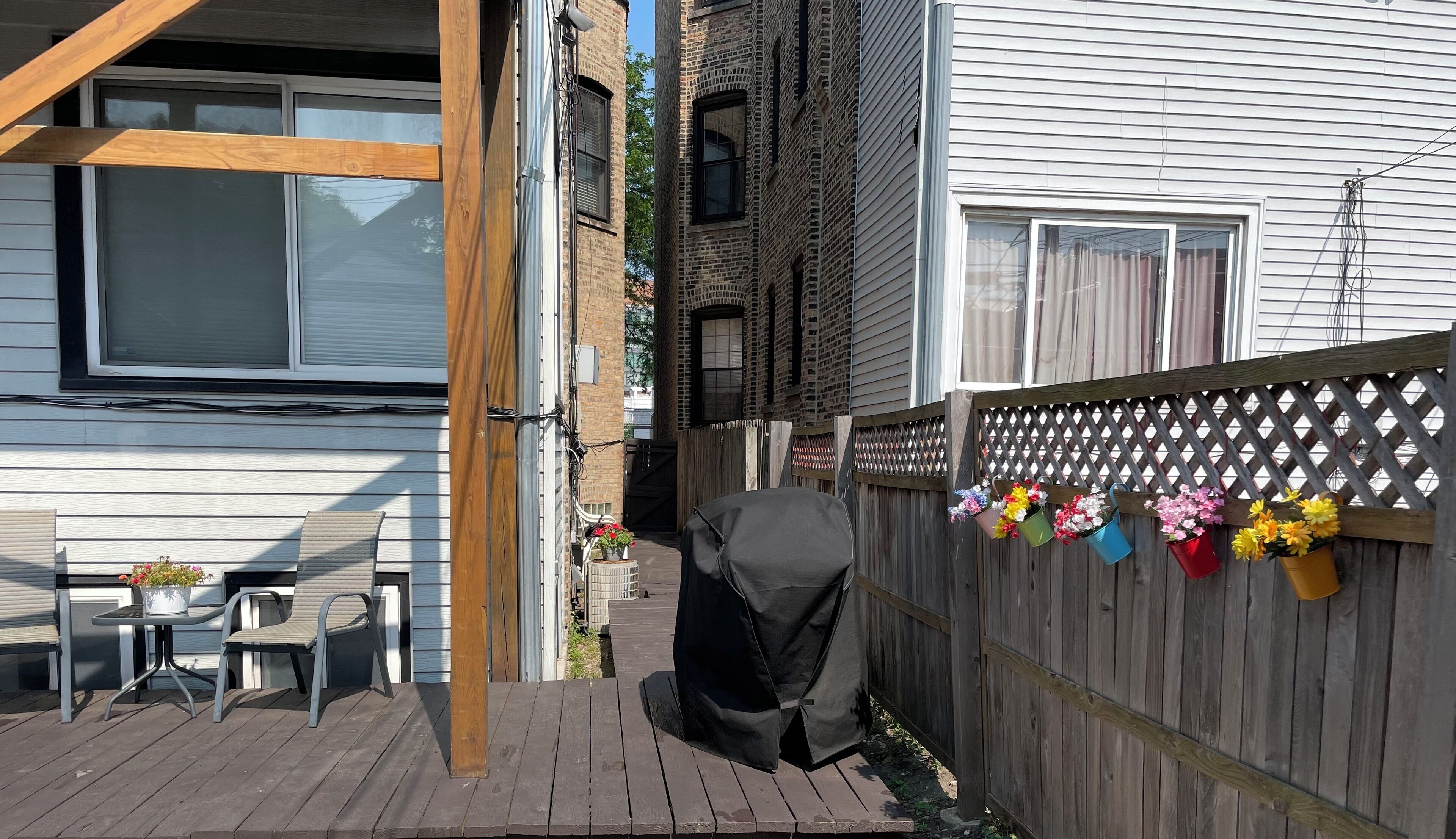 A wooden deck with a covered grill, a table with chairs, and a wooden fence with flower pots.
