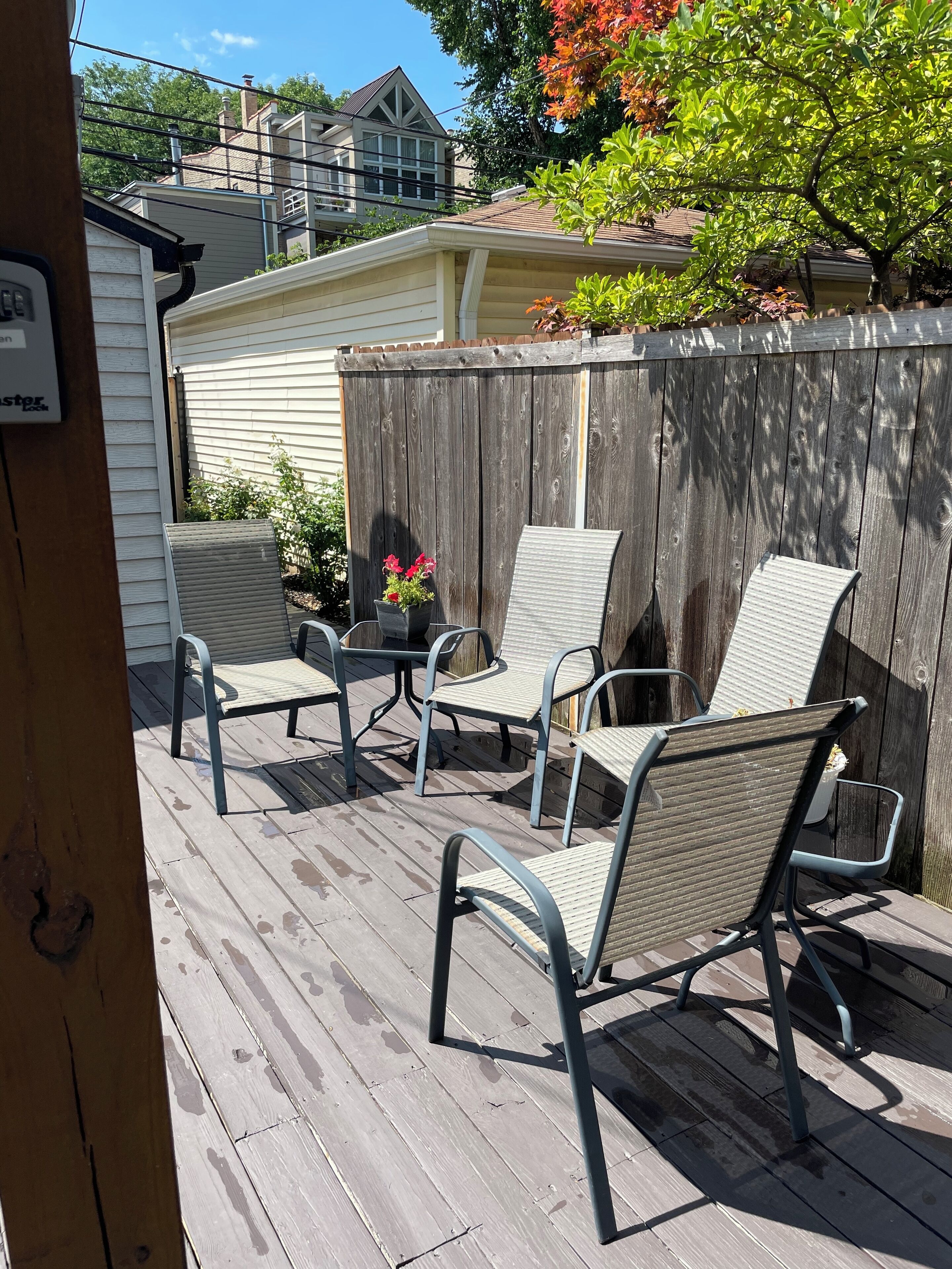 Una terraza de madera con cuatro sillas de metal y una mesa, rodeada por una valla de madera.