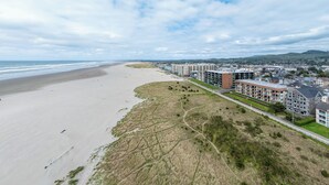 An aerial view of a coastal area with a beach, a road, and residential buildings. - Sweeping oceanfront views from this one bedroom condo right on the prom! (Seaside)