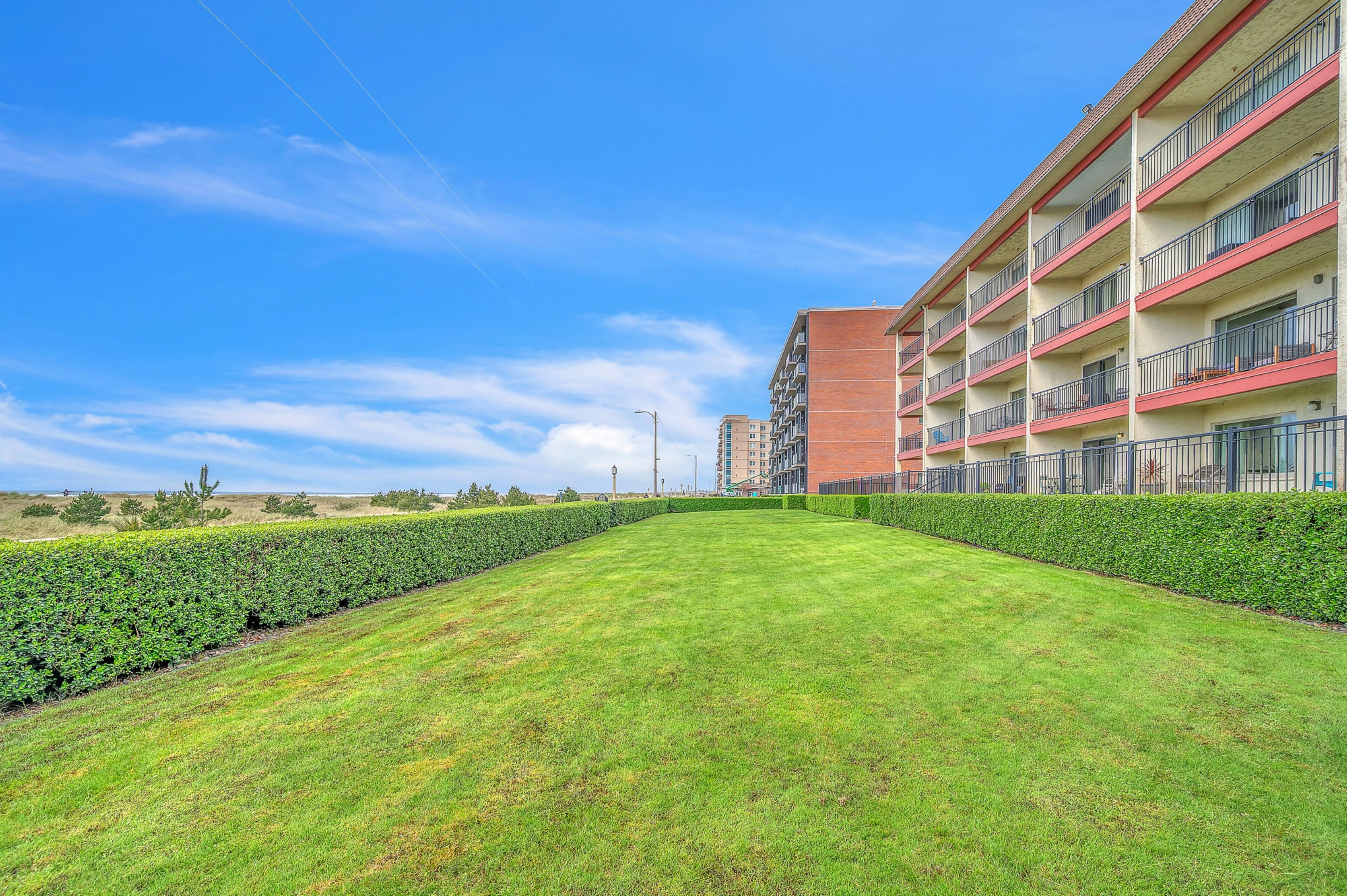 A well-maintained lawn, a multi-story building with balconies, and a clear blue sky.