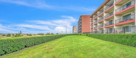 A well-maintained lawn, a multi-story building with balconies, and a clear blue sky.
