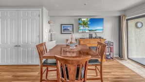 Zona pranzo con tavolo e sedie in legno, un quadro raffigurante una spiaggia e una libreria.