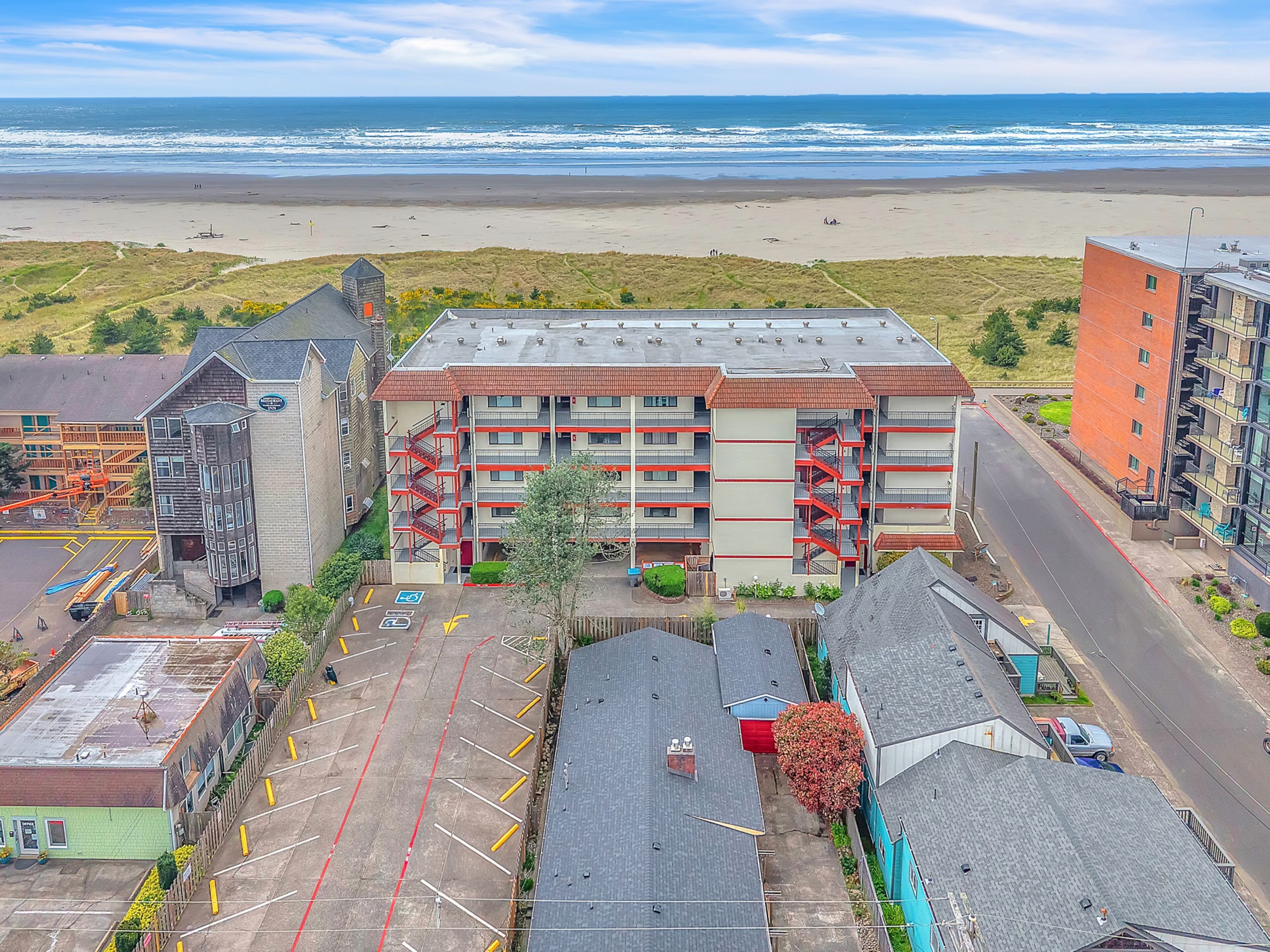 A multi-story hotel with a parking lot, a beach view, and a road in the foreground.