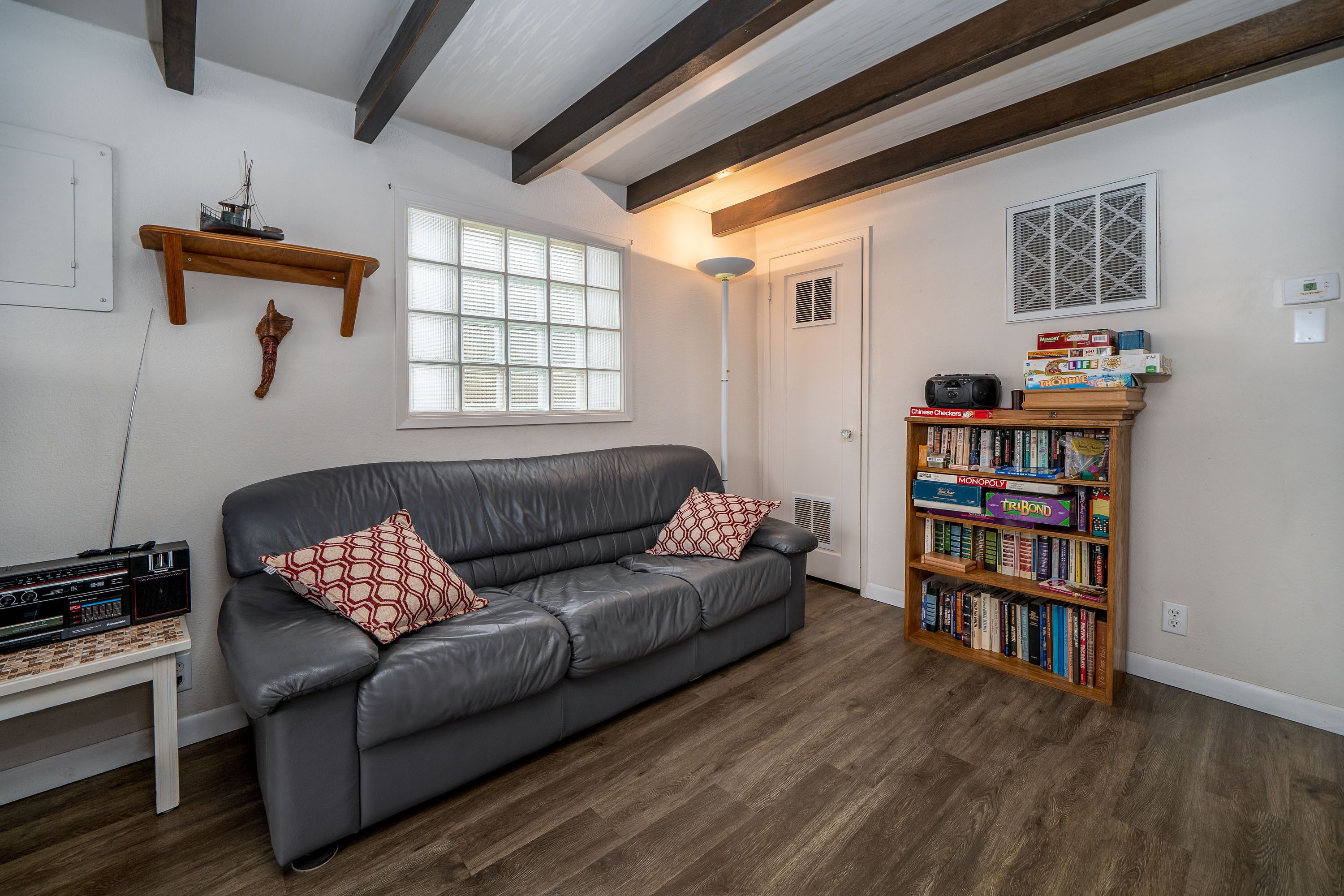 Ein Wohnzimmer mit einem grauen Ledersofa, einem Bücherregal mit Gesellschaftsspielen und einem Fenster mit Jalousien.