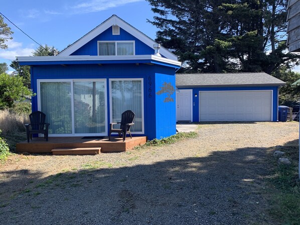 A small blue house with a garage, two chairs outside, and a gravel driveway.