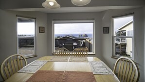 Ein Esszimmer mit einem großen Tisch, vier Stühlen und zwei großen Fenstern mit Blick auf eine Wohngegend.