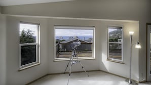 Ein Zimmer mit drei großen Fenstern, einem Teleskop und einer Stehlampe.
