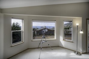 A room with three large windows, a telescope, and a floor lamp.