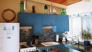 A modern kitchen with blue cabinets, a white refrigerator, a stove, and a sink. - Oceanfront Cottage with Deck and Ocean Views, Dogs Ok, Perfect Couples Retreat (Seal Rock)