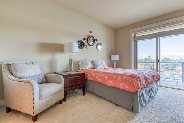 A bedroom with a bed, a chair, a nightstand, and a window with a view.