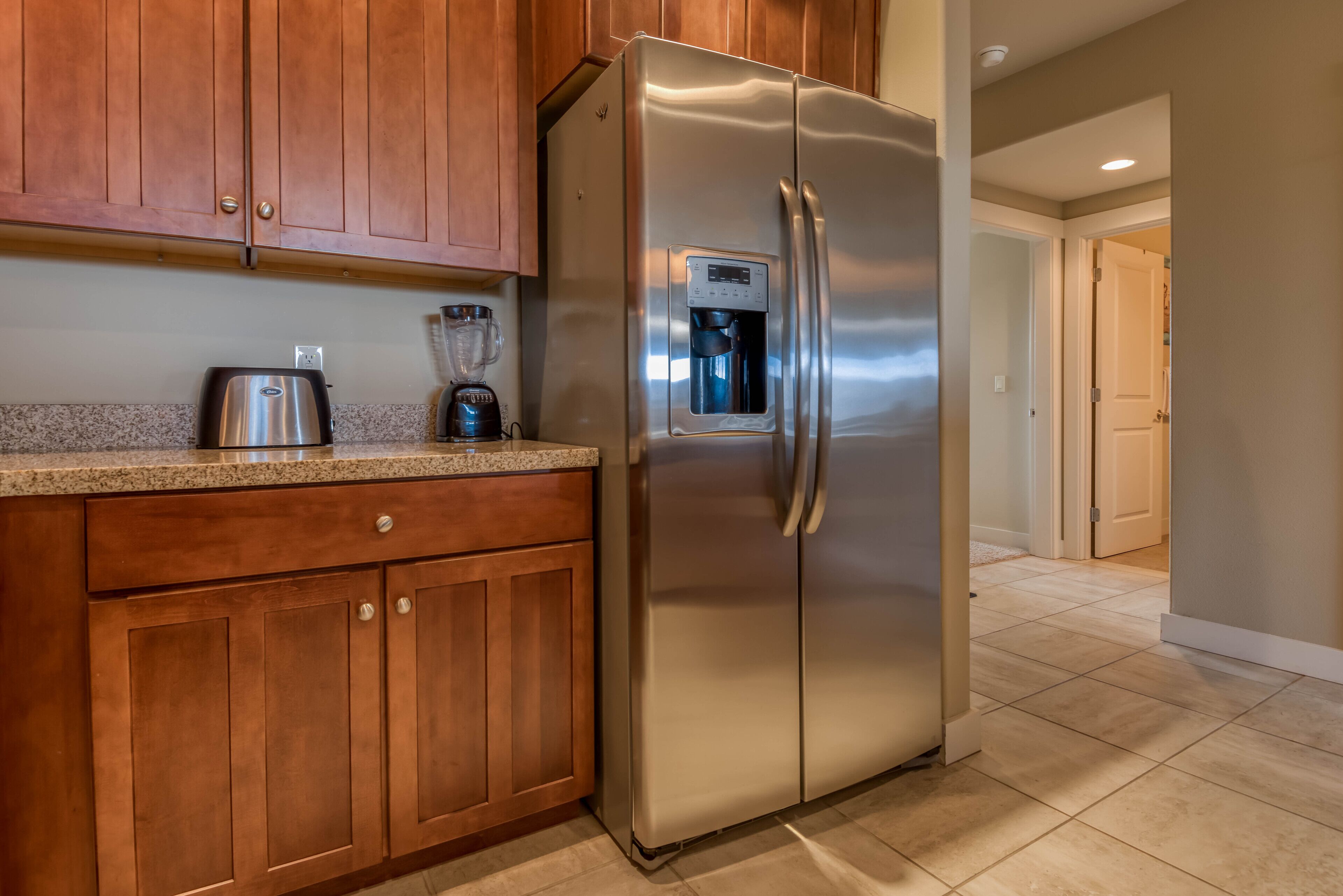 A kitchen with wooden cabinets, a stainless steel refrigerator, a coffee maker, and a blender.