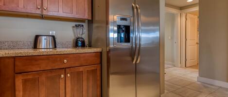 A kitchen with wooden cabinets, a stainless steel refrigerator, a coffee maker, and a blender.