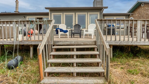 Une terrasse en bois avec un escalier menant à un espace abrité comprenant deux fauteuils Adirondack et une table.