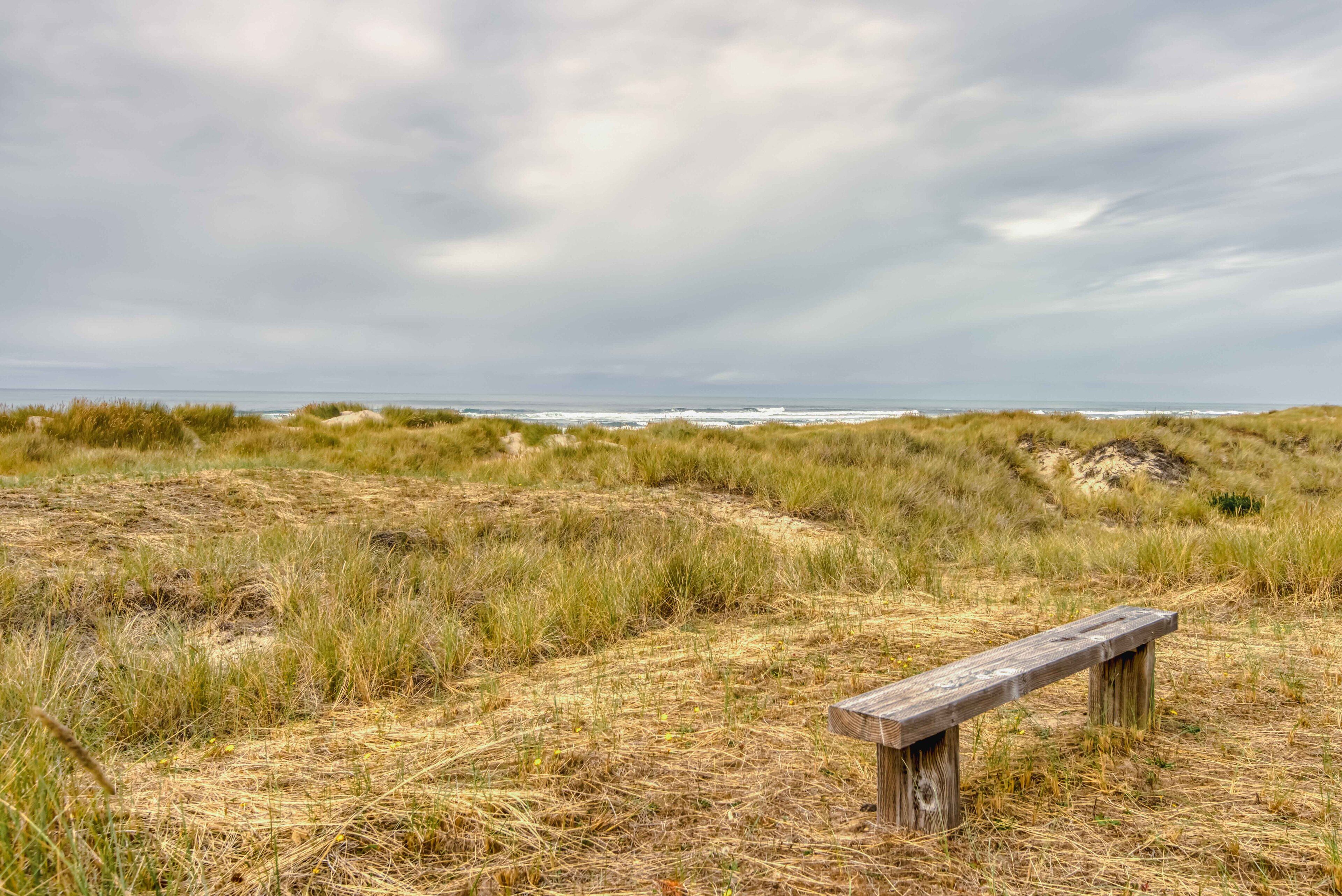 Eine Bank in einer grünen Landschaft mit Blick auf das Meer unter einem bewölkten Himmel.