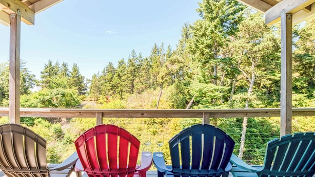 Een houten terras met Adirondack-stoelen en een tafel, met uitzicht op een bebost gebied.