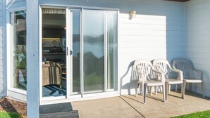Eine überdachte Terrasse mit einer Glasschiebetür, die zu einem Küchenbereich führt, zwei weiße Plastikstühle und ein kleiner Terrassenheizer.