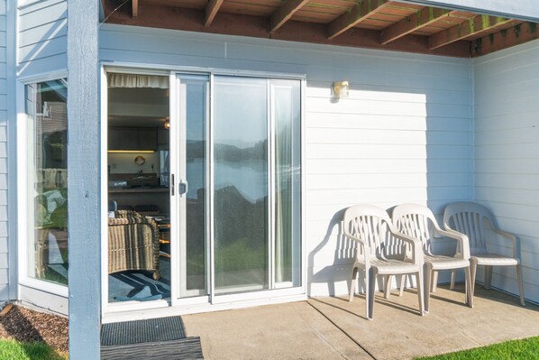 A covered patio with a sliding glass door leading to a kitchen area, two white plastic chairs, and a small outdoor heater. - Beach Getaway! Oceanfront, amazing views, beach access and sleeps up to 5 (Lincoln City)