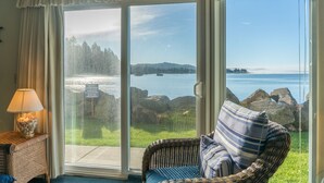 Ein Zimmer mit einer großen Schiebetür, die zu einem malerischen Seeblick führt, ein Korbstuhl mit gestreifter Sitzkissen und eine Lampe auf einem Beistelltisch.