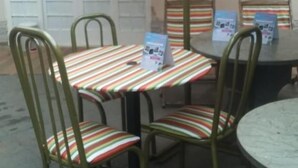 A table and chairs with a striped tablecloth, a metal umbrella, and a wall with a door. - Pousada Vale das Águas (Foz do Iguaçu)