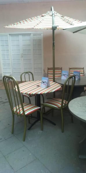 A table and chairs with a striped tablecloth, a metal umbrella, and a wall with a door. - Pousada Vale das Águas (Foz do Iguaçu)
