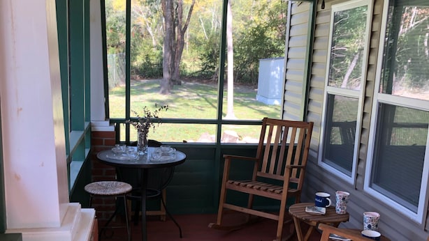 Eine überdachte Veranda mit Tisch und Stühlen, einem Deckenventilator und Blick auf den Garten.