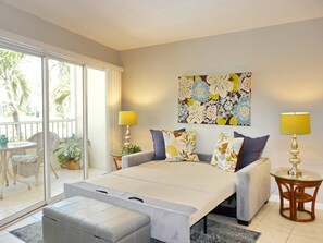 Un dormitorio con cama, dos lámparas de noche, un cuadro grande con motivos florales y un balcón con sillas y plantas.