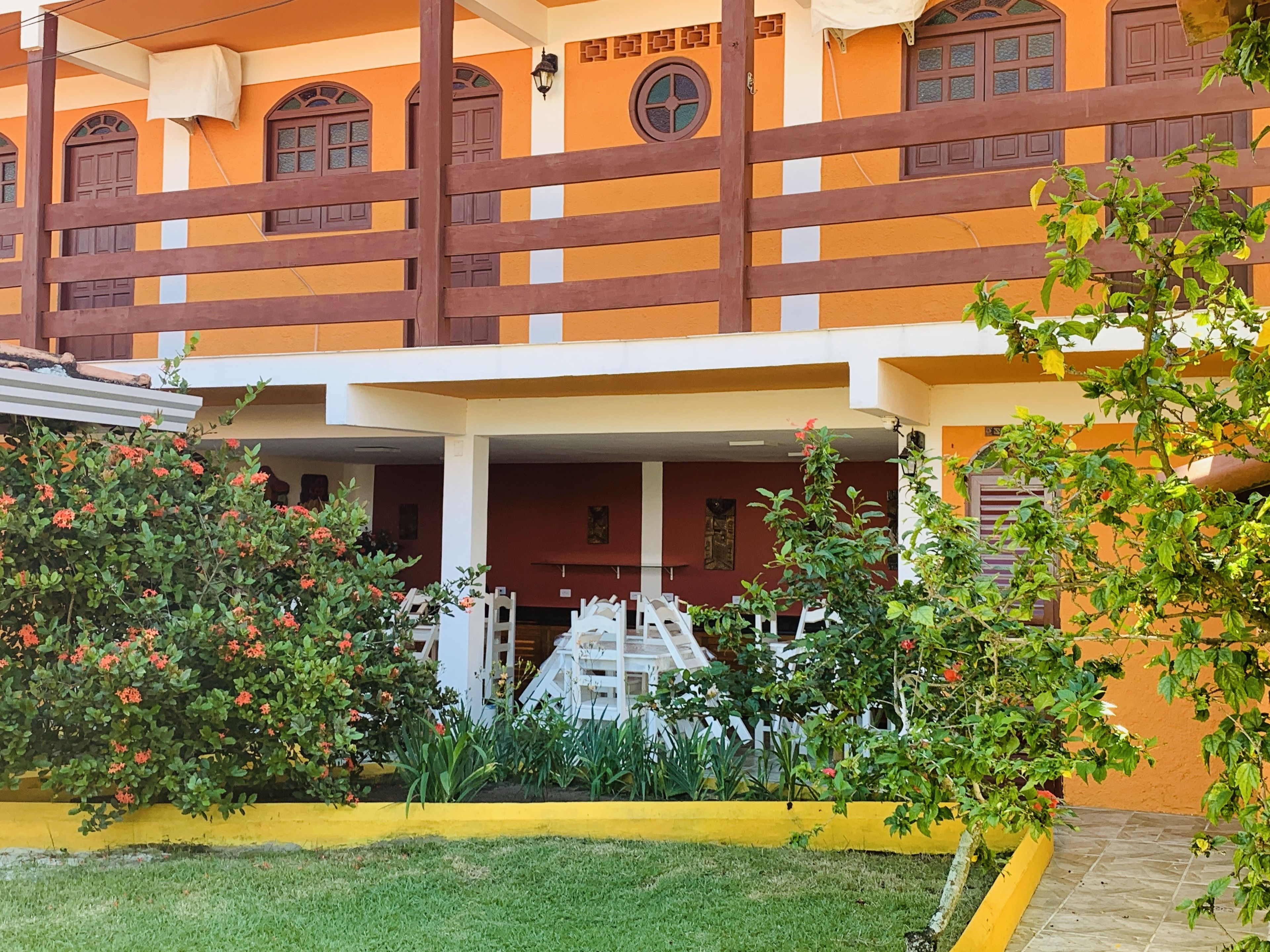 A building with a yellow facade, a wooden fence, and a covered entrance area with a white railing.