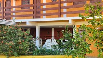 A building with a yellow facade, a wooden fence, and a covered entrance area with a white railing.