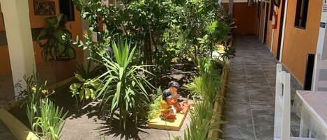 Un patio con un pequeño estanque, rodeado de diversas plantas y una estatua.